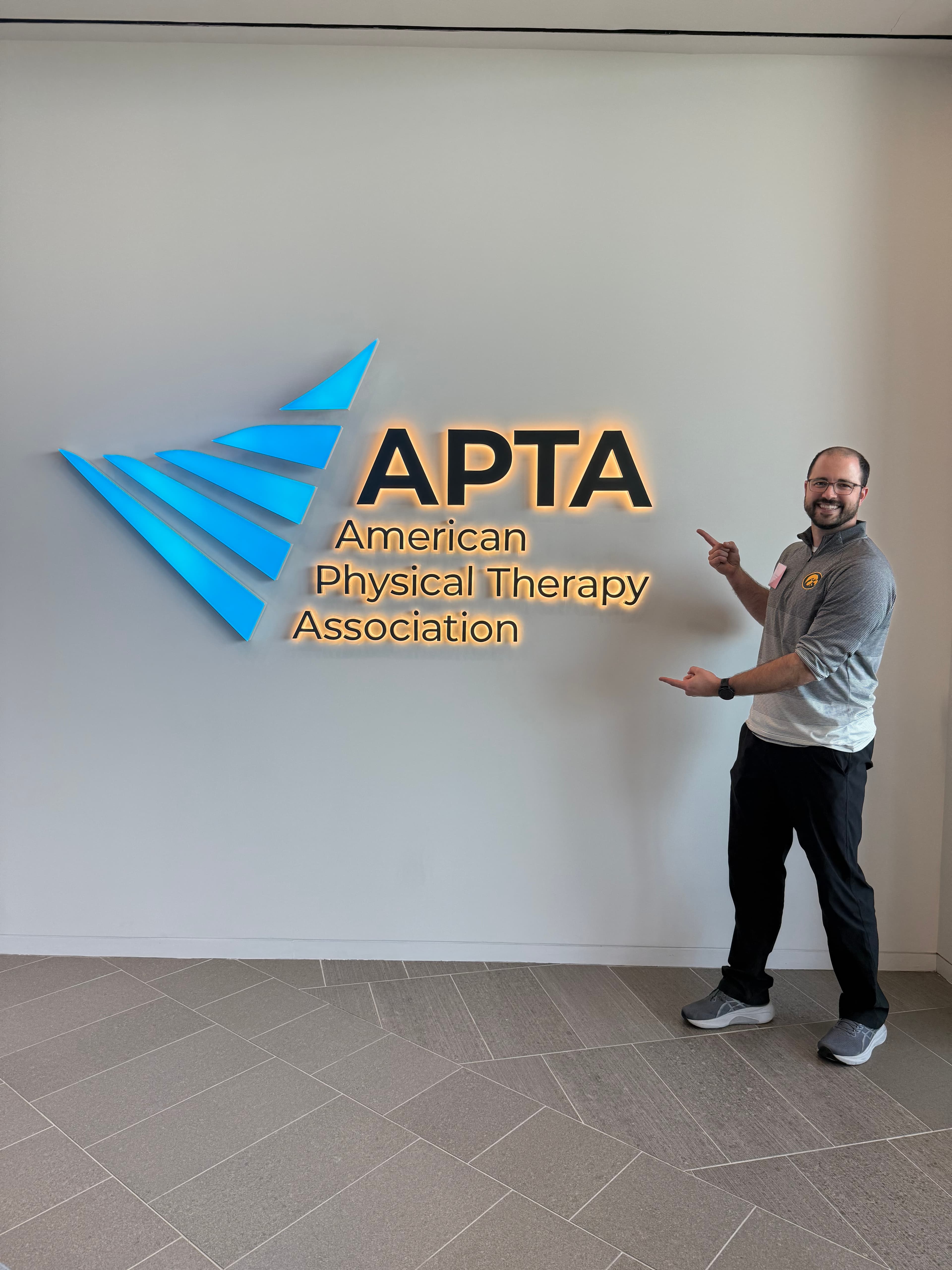 Aero Performance and Physical Therapy team member standing beside an illuminated APTA (American Physical Therapy Association) sign inside the clinic